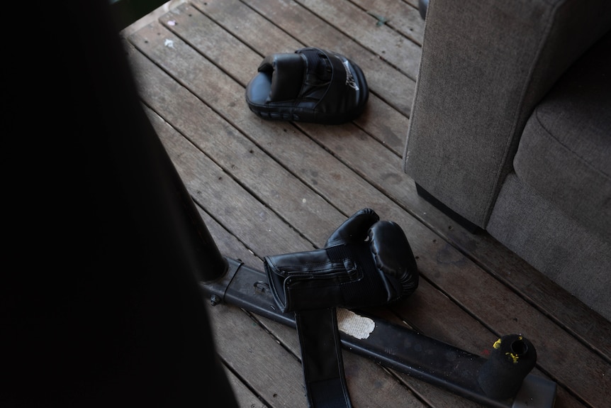 Black child-sized boxing gloves and pads lay on the veranda floor next to an worn grey couch