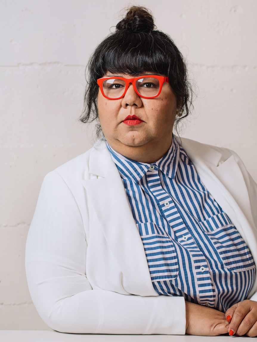 A portrait of a woman wearing striking red glasses and a white blazer.