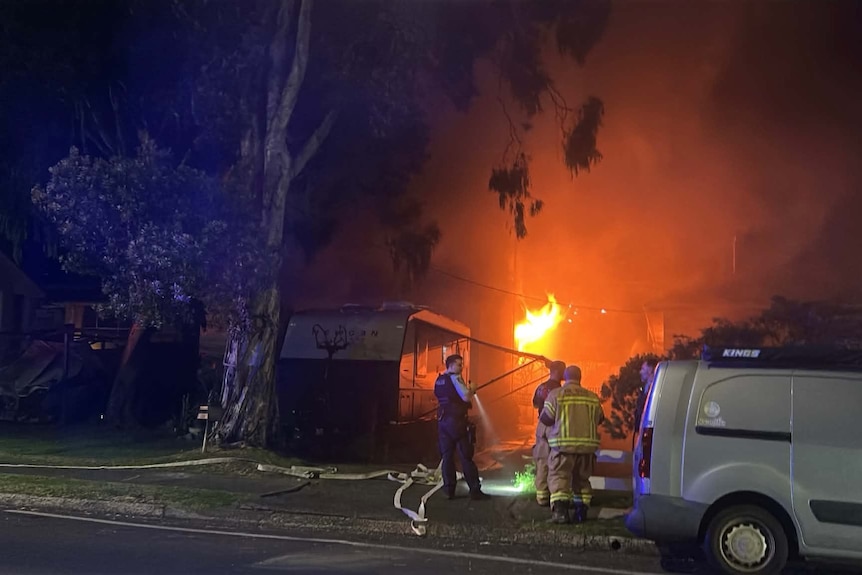 Firefighters putting out a fire on a residential street at night.