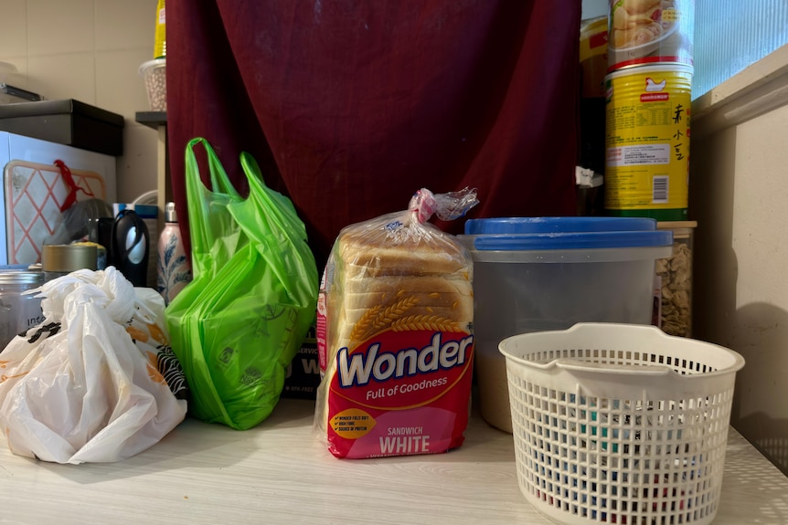 Groceries on a kitchen bench including a loaf of white bread.
