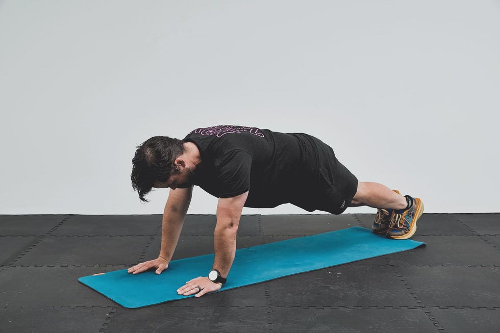 Person performing a plank exercise on a blue mat in a gym setting.