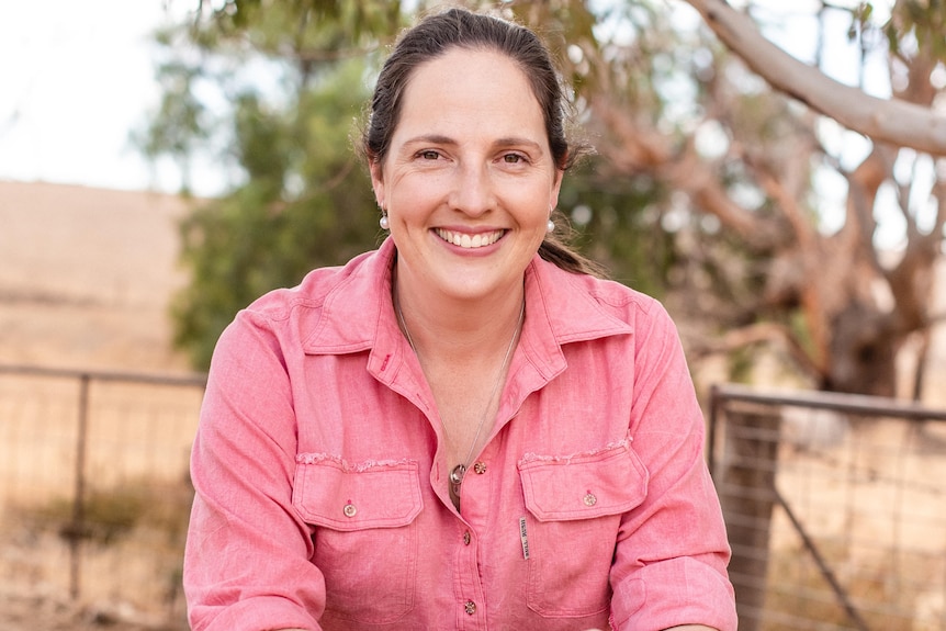 woman in red shirt leaning on a fence in rural area