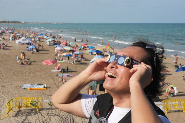 A man wears special eclipse glasses, as beachgoers gather before a total solar eclipse set to begin around sunset, at a beach near Valencia, Spain, Wednesday Aug. 12, 2026. (AP Photo/Alberto Saiz)