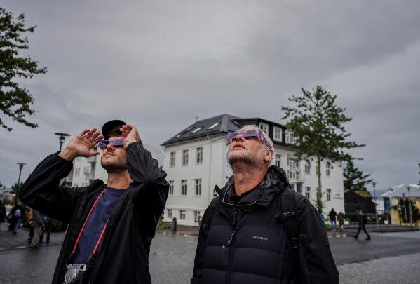People use solar eclipse glasses to look up at the sun ahead of a solar eclipse Reykjavik, Iceland, Wednesday, Aug. 12, 2026. (AP Photo/Marco di Marco)