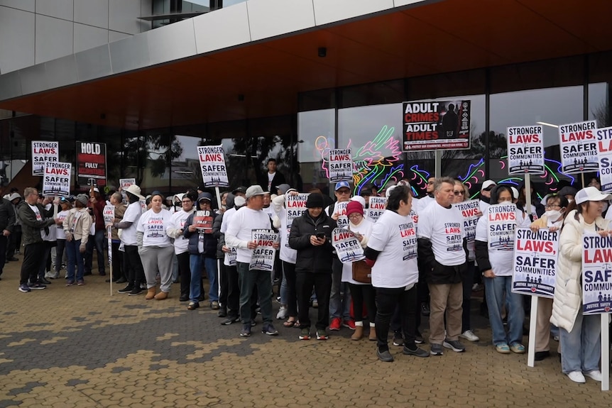 People in white shirts and caps stand with signs saying "stronger laws, safer communities".