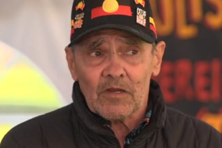 Robbie Thorpe talks to the camera wearing a cap with the Aboriginal flag
