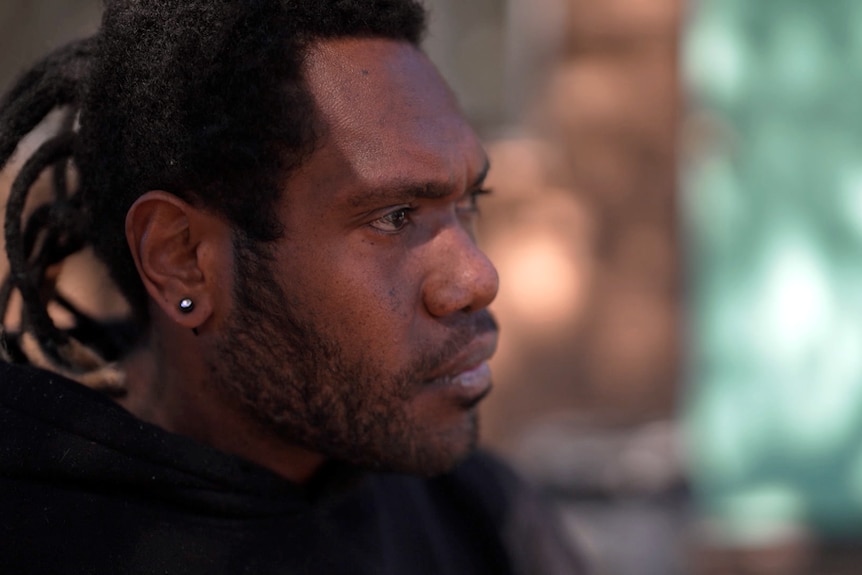 A man looks to the side of frame with a serious expression.