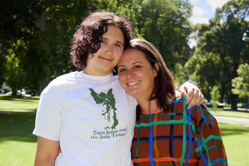 Simone Kelly and stepson Eli stand outside and hug while facing the camera.