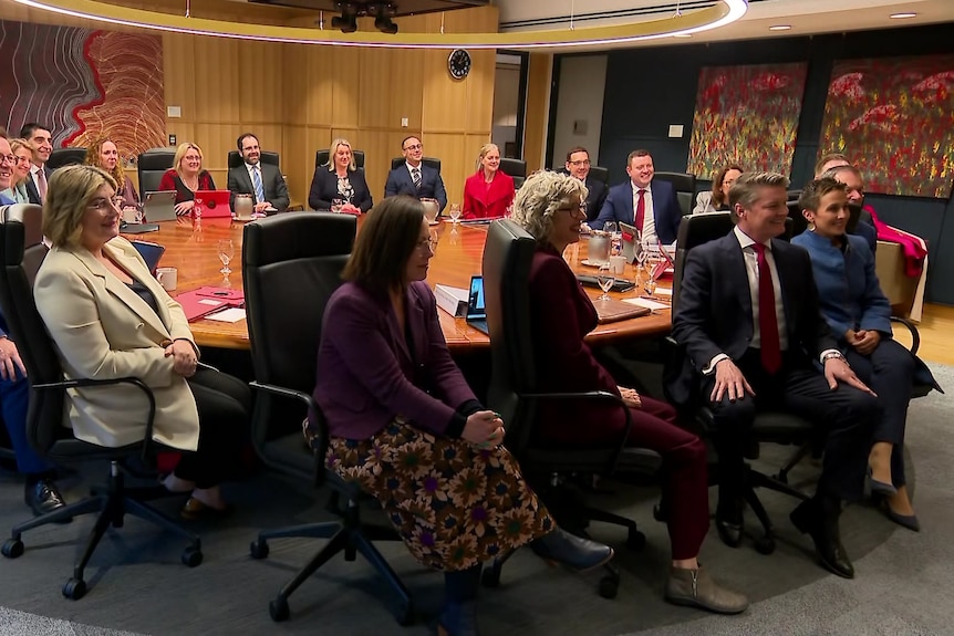 Men and women in suits sit around a round table, smiling for a photographer.