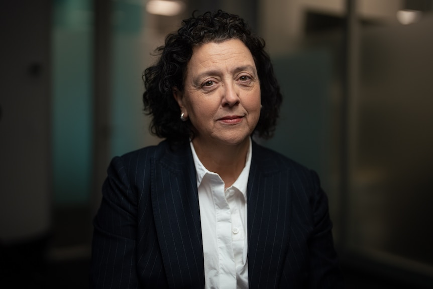 a female politician with short dark brown curly hair wearing a navy blazer and white collared shirt looking serious