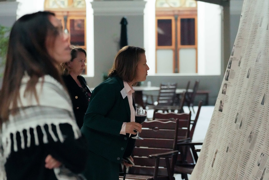 A group of women look at a huge paper that lists the names of thousands of children in parliament