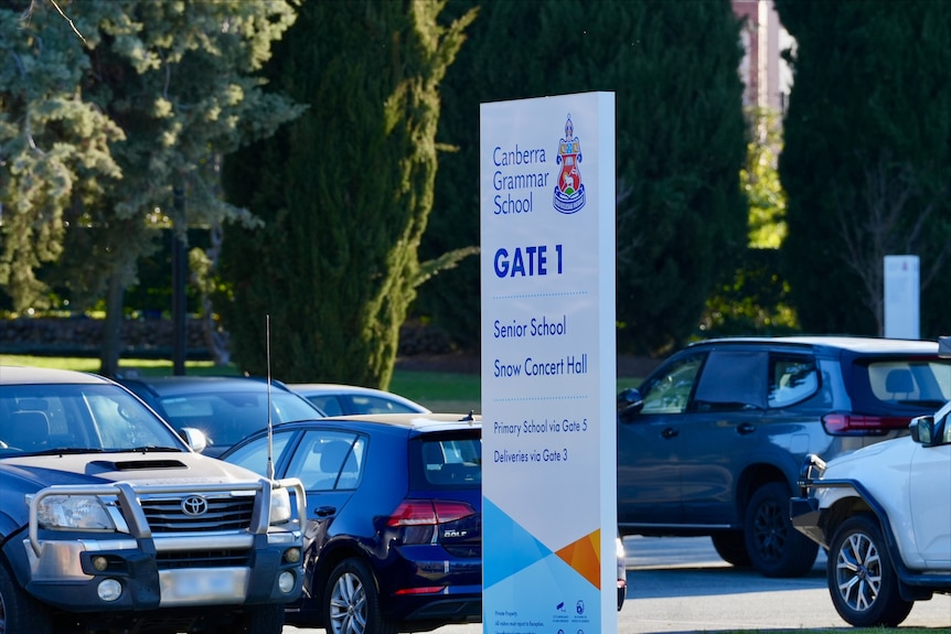 Cars in a parking lot near a sign for Gate 1 to Canberra Grammar School.