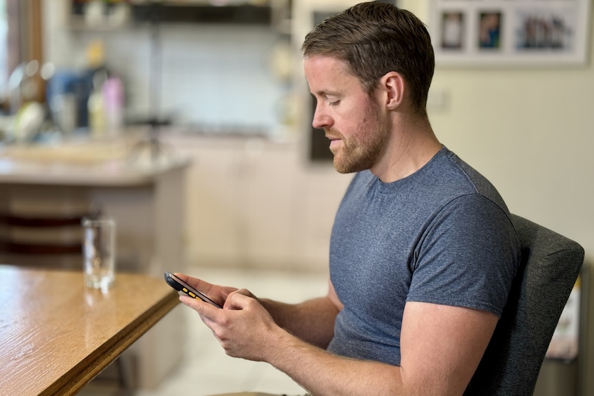 A side profile of a man in a grey t-shirt typing on a smart phone.