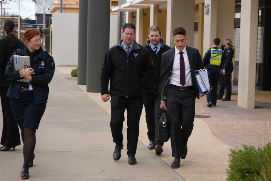 A man in a suit surrounded by uniformed police officers