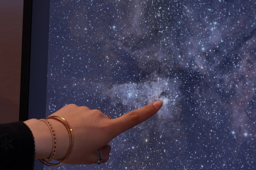 A woman's hand pointing on a screen which shows a space galaxy.
