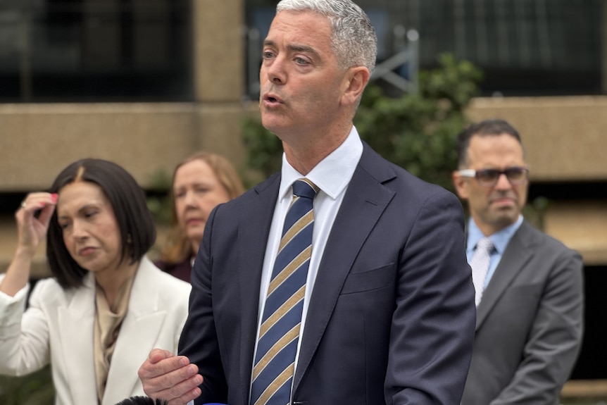 Chris Minns at mic wearing green tie