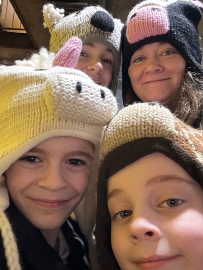 A woman and three boys all wearing novelty beanies crowd into a selfie-style picture.