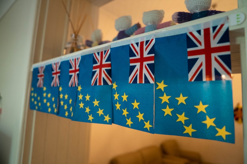 Tuvaluan flags with a blue background, yellow stars and the Union Jack, hang in a row.