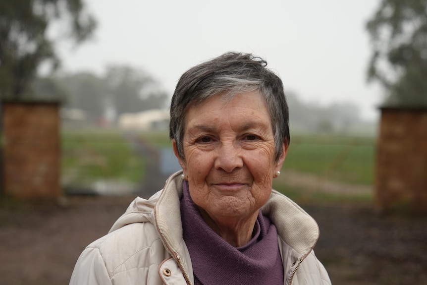A woman stands outside property gates of a country proprety on a misty day.