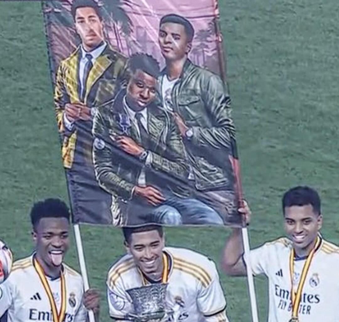 Bellingham, Vinicius, and Rodrygo posing with the Supercopa and a fan’s poster