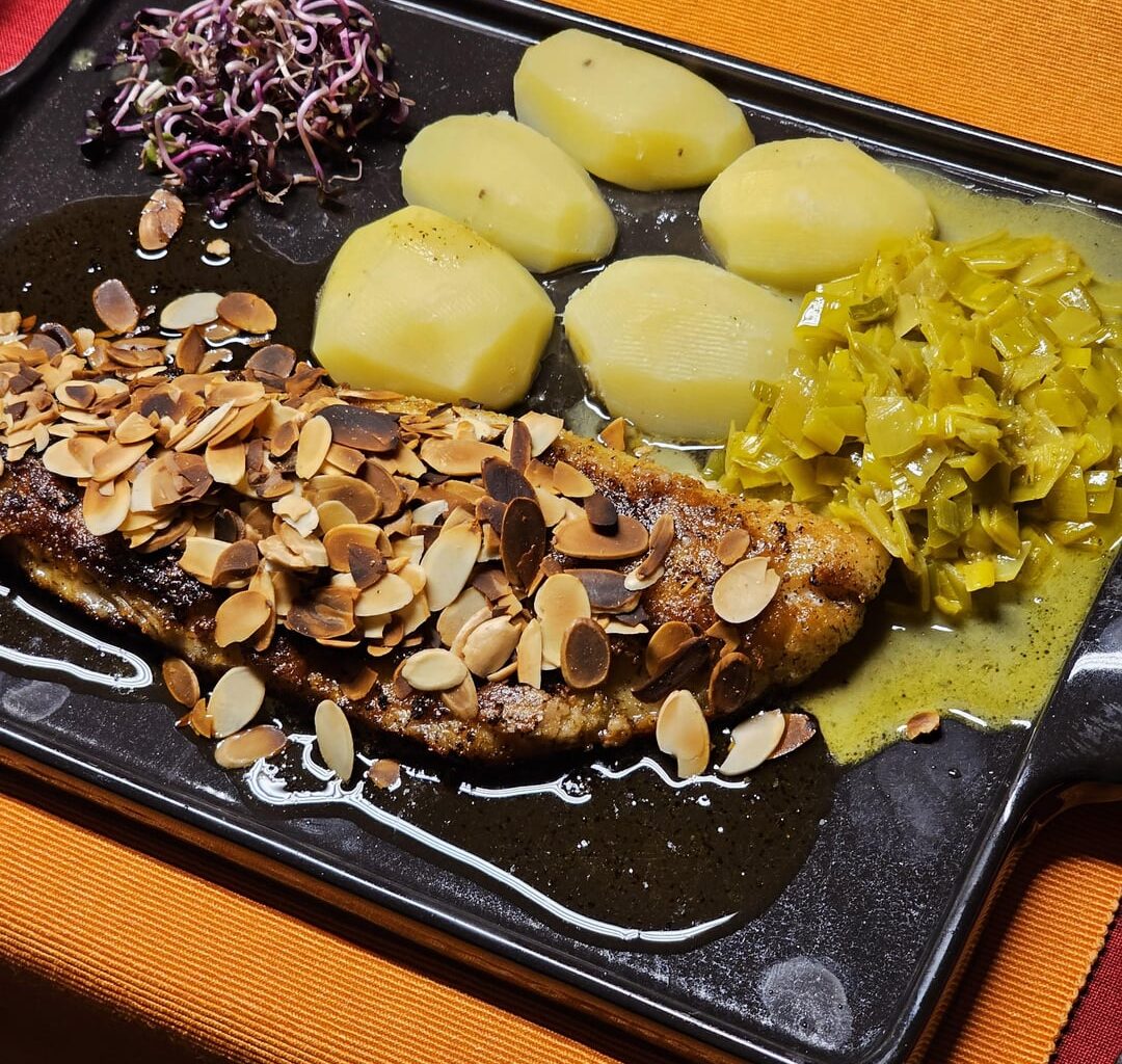 Fried fillet of pike-perch with roasted almonds in a lemon-butter sauce, with leek in a curry-white wine sauce, boiled potatoes and red radish sprouts