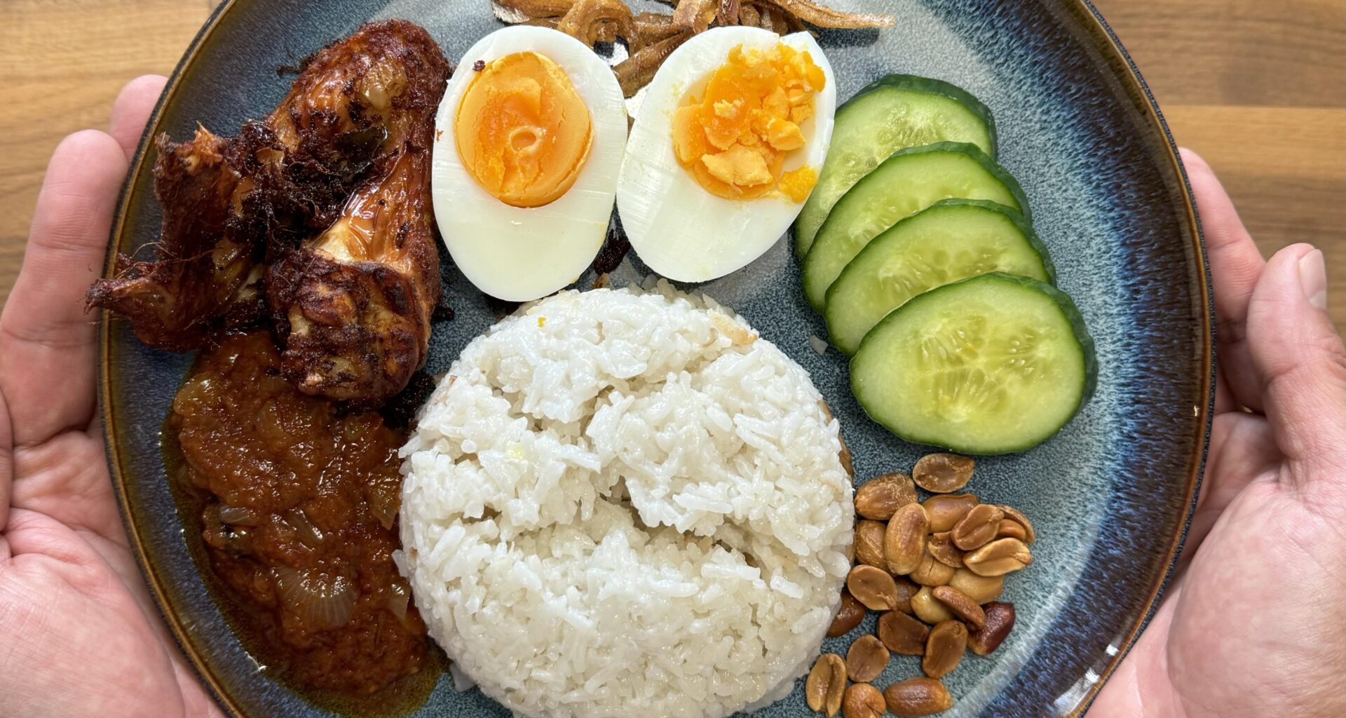 Nasi Lemak, a Malaysian local dish. Coconut rice infused with Pandan, homemade sambal, spiced chicken, boiled eggs, fried anchovies, cucumber and toasted nuts.