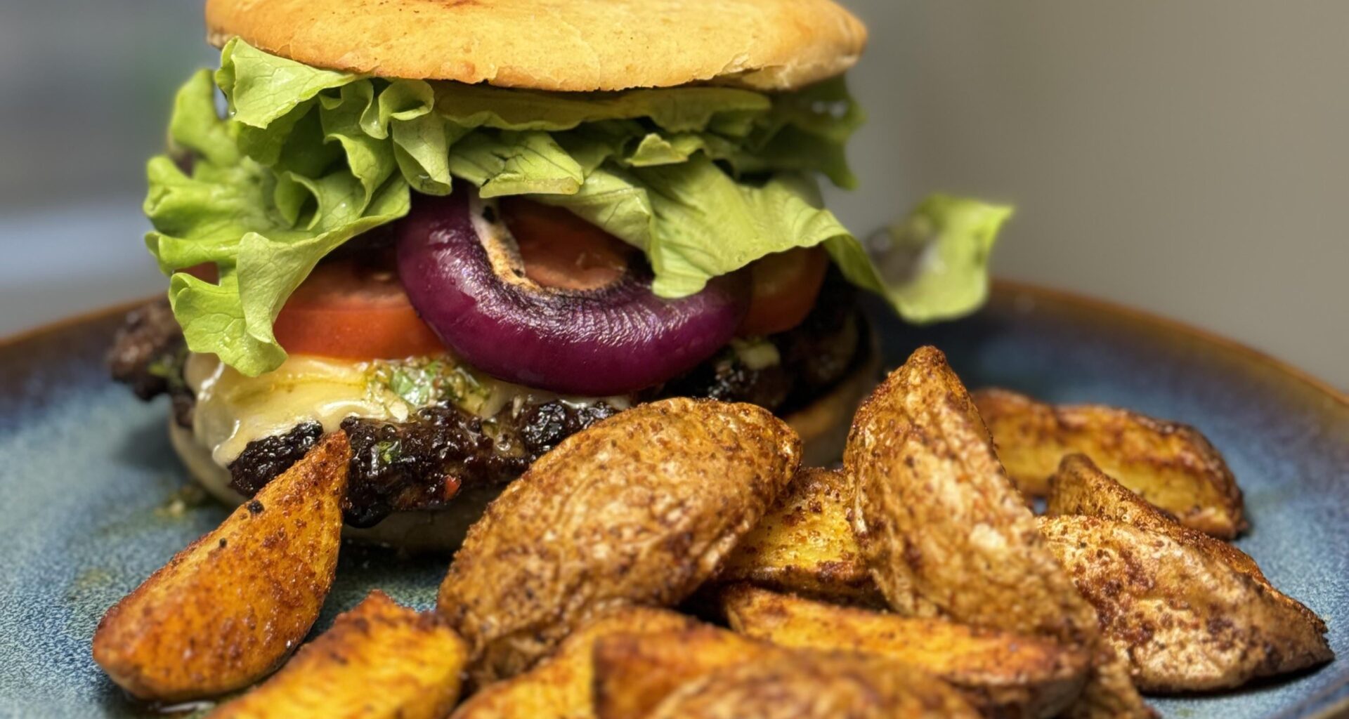 Homemade beef burger with chimichurri, cheddar, tomato, roasted onion and air fried potatoes