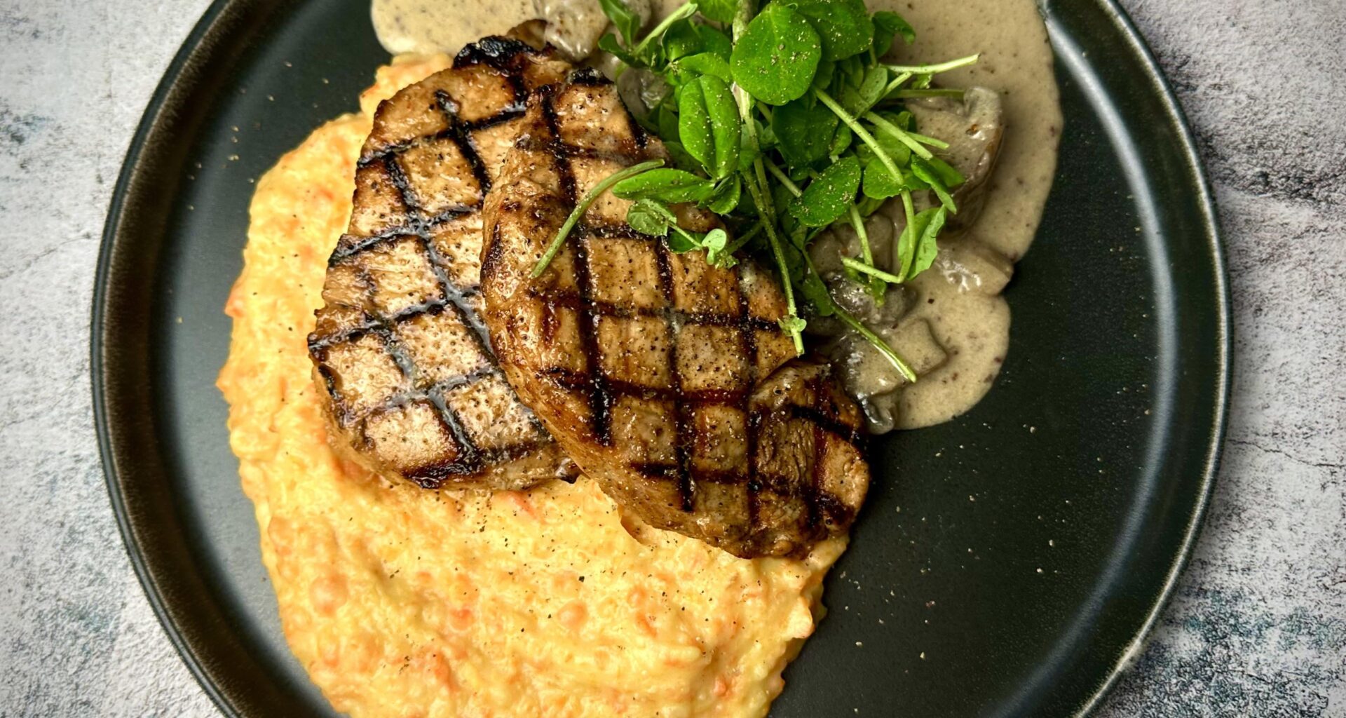 Grilled pork chops on mashed potatoes & carrots served with mushrooms stewed in a cream sauce with horseradish