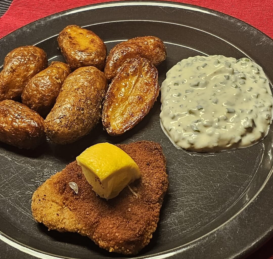 Schnitzel, accompanied by fried potatoes and a homemade chive-based sourcream sauce as a dip with the potatoes
