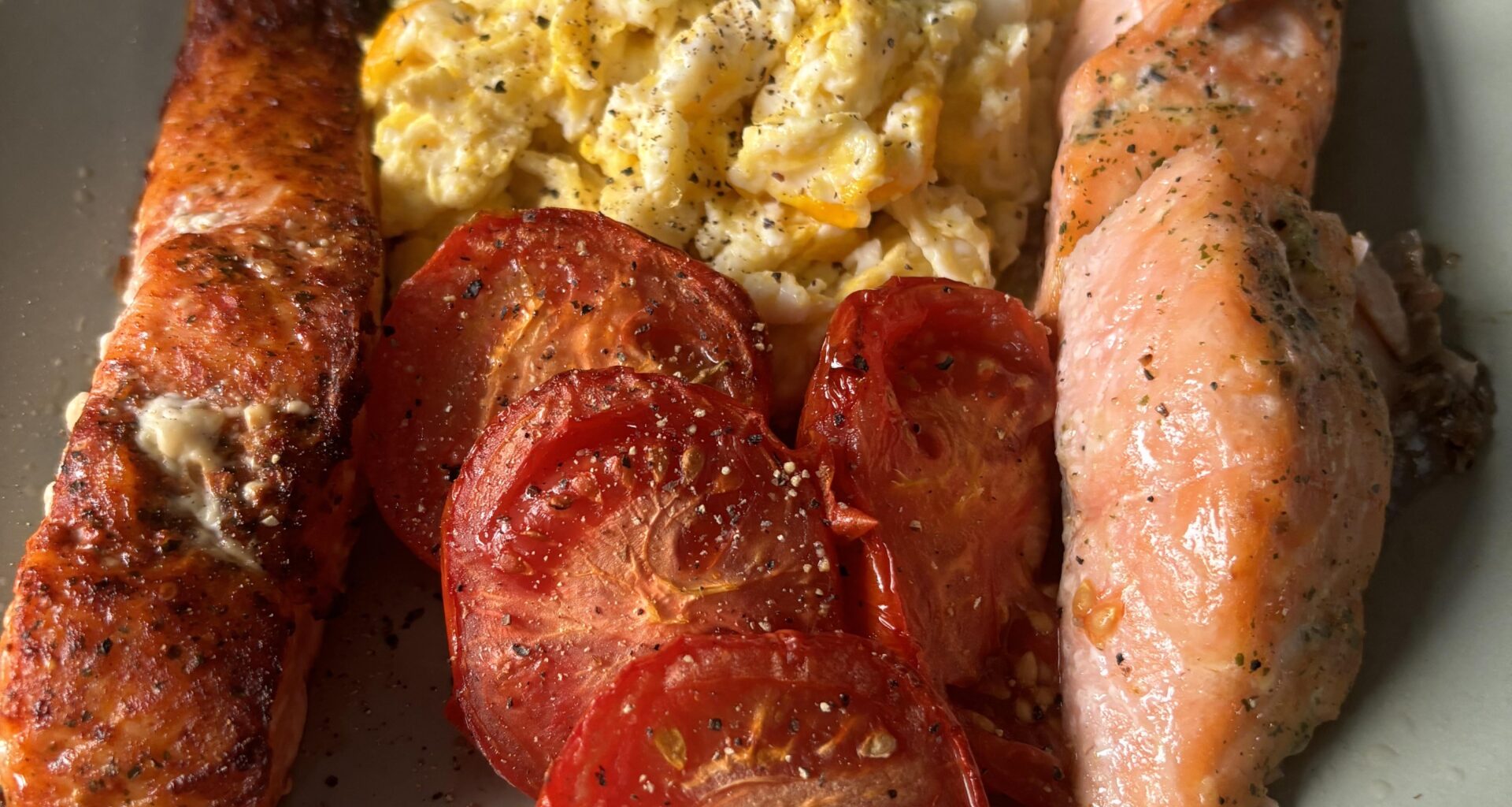 Harissa and lemon garlic salmon fillets with scrambled eggs and grilled tomatoes.