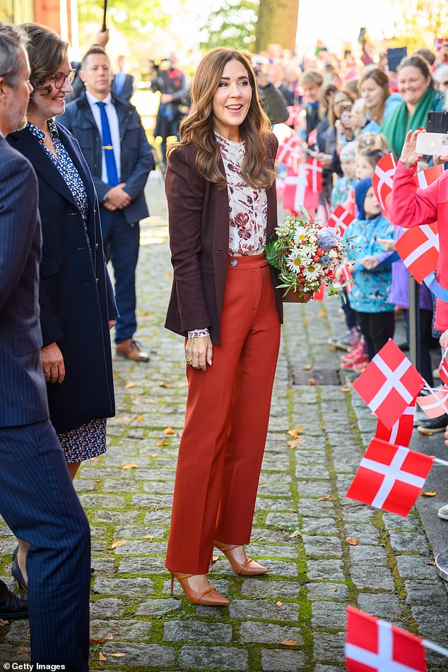 Queen Mary wears a striking pair of burnt orange tailored trousers and a burgundy blazer to visit the Schleswig-Holstein state government building today in Kiel