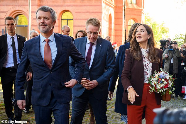 Her husband King Frederik (left) looks dapper in a pin-stiped navy suit complete with a crisp light blue shirt, black polished shoes and an amber coloured patterned tie