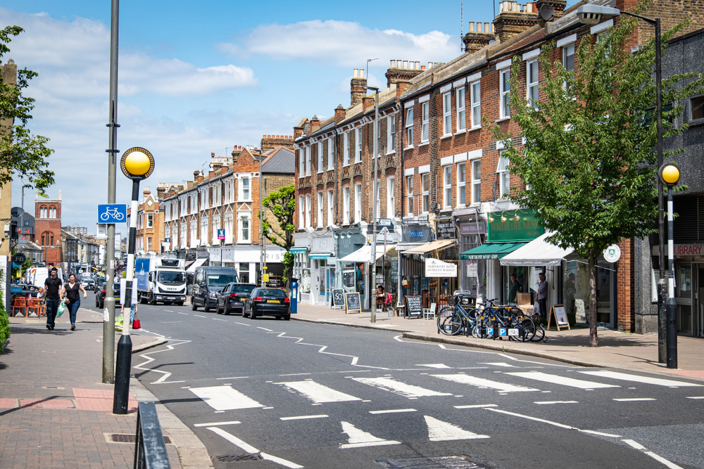 Clapham on a sunny day, with red brick buildings on the high street and a zebra crossing.