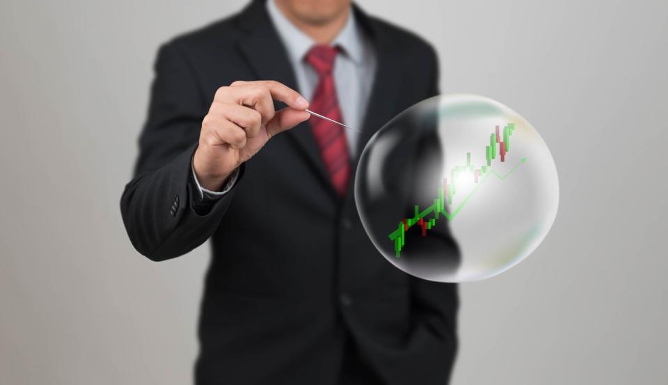 An investor holding a pin to pop a bubble with a stock chart in it.