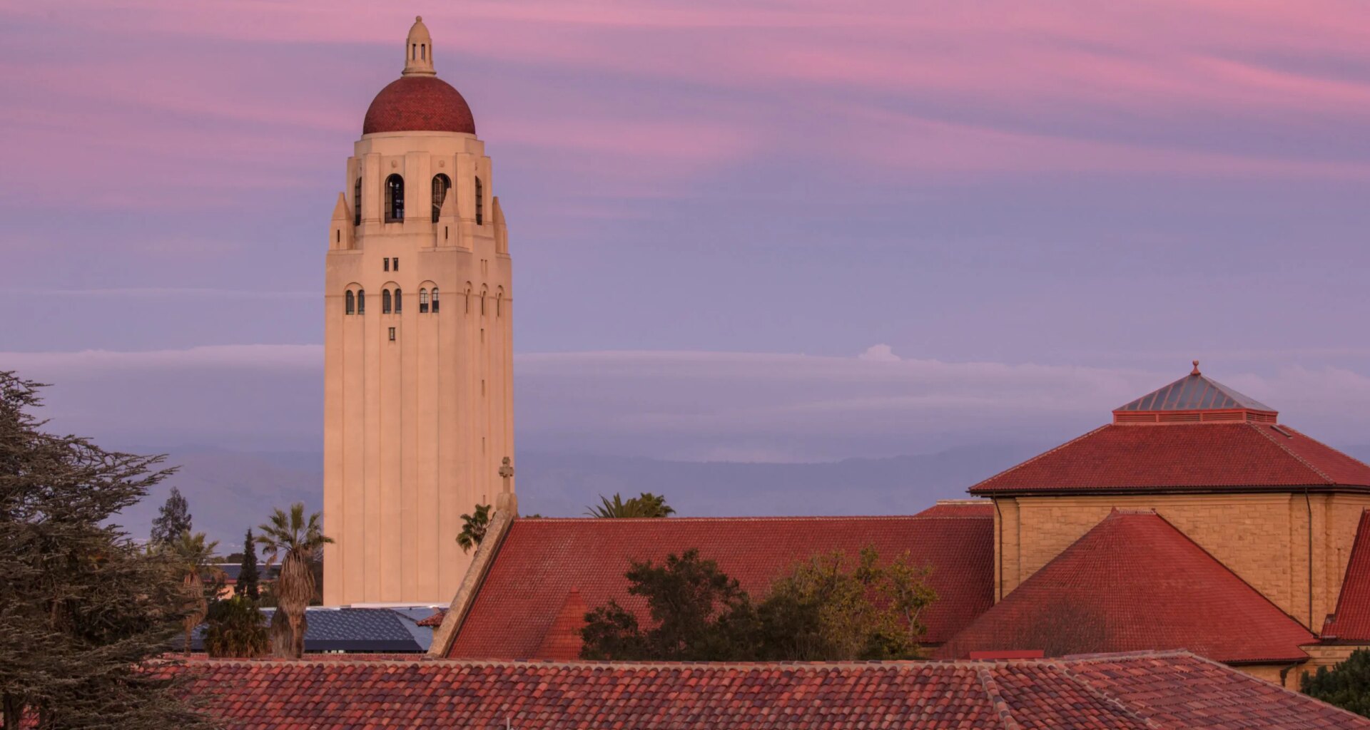 Hoover Tower above sandstone buildings, purple and pink sky in the background