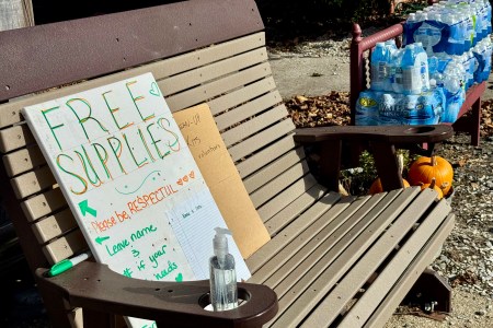 Shows a sign on a bench inviting people take supplies that have been donated for victims of Hurricane Helene in Spruce Pine, North Carolina. Packages of bottled water are seen next to the bench.