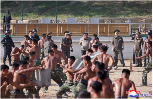 North Korean troops in combat training with their shirts off. Kim Jong Un stands behind them in the background.