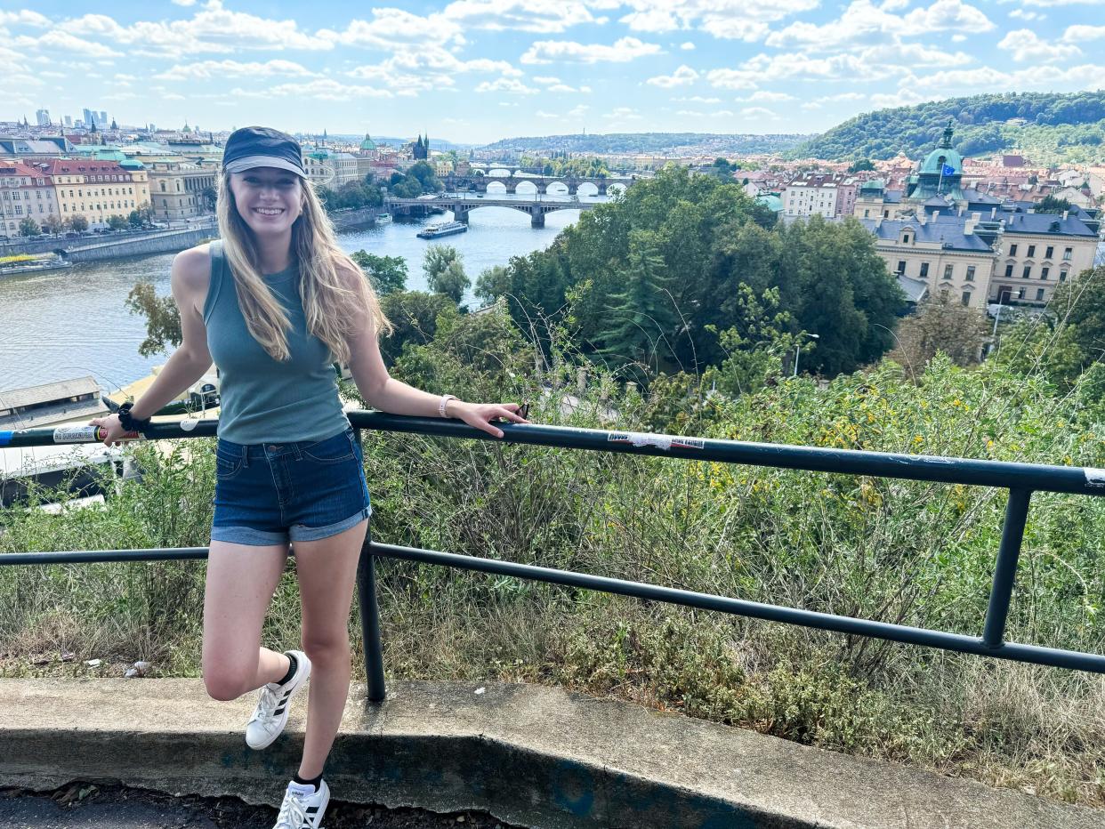 The author poses near a lookout in Prague, with buildings, trees, and brides behind her.