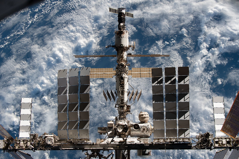 Space station leak: The space station with modules and solar panels all hooked together above a cloudy Earth.