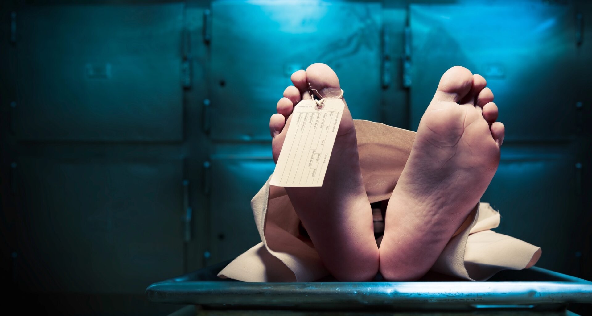 a body on a morgue table with only the feet showing and a toe tag on the big toe