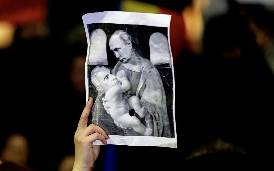A Romanian activist holds up a placard depicting Romanian far-right independent candidate Calin Georgescu (L) and Russian President Vladimir Putin