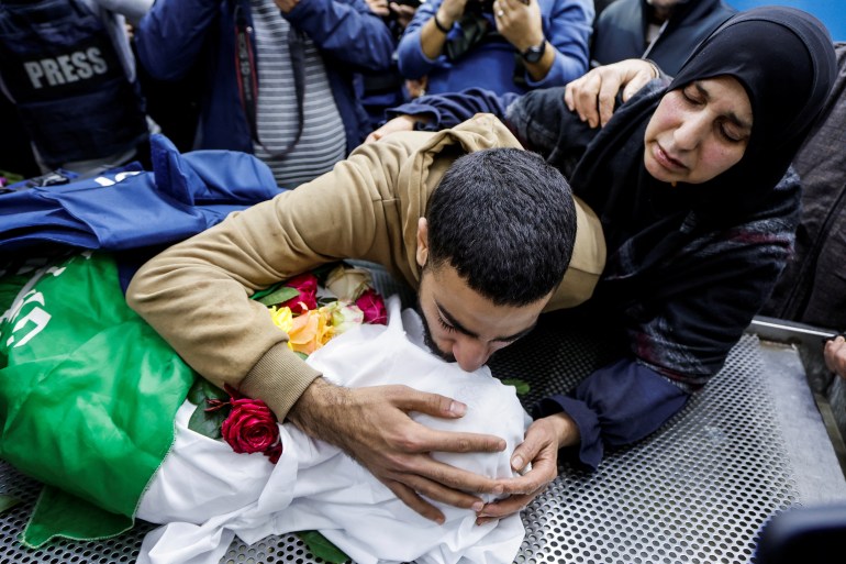 a man wearing brown kisses the body of a woman wrapped in white with flowers