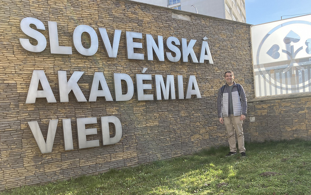 JD Mendez in front of a sign reading Slovenska Akademia Vied