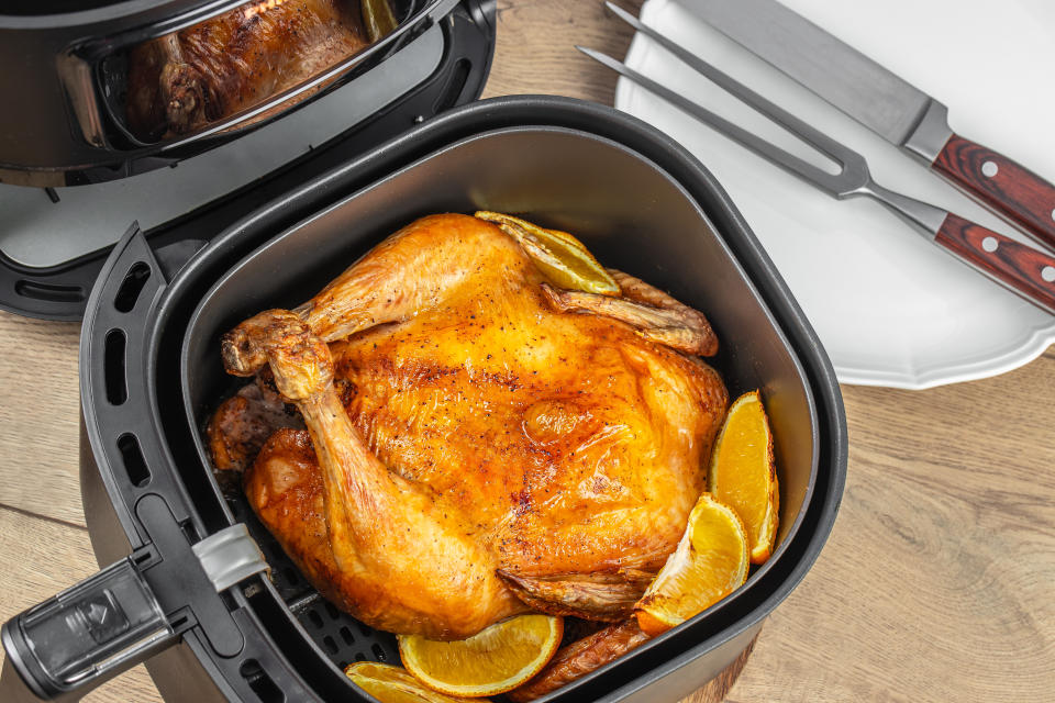 delicious roasted whole chicken with oranges in air fryer on a wooden table. top view.�