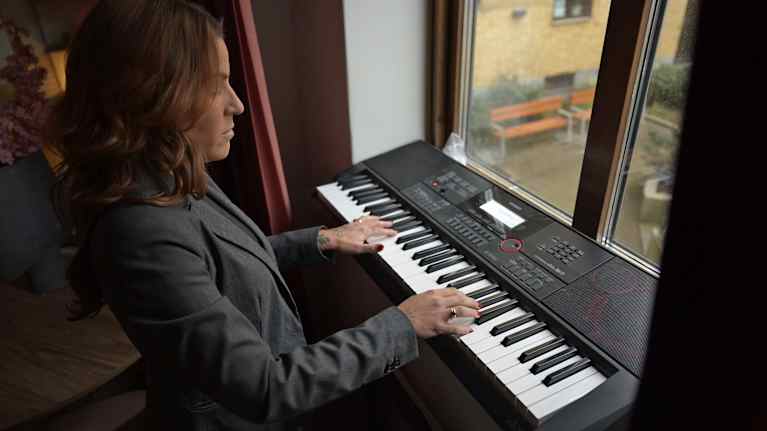 En kvinna spelar piano invid ett fönster.