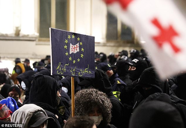 A demonstrator holds a placard reading "We are here" during a protest against the new government's decision to suspend the European Union accession talks and refuse budgetary grants until 2028, in Tbilisi, Georgia November 30, 2024