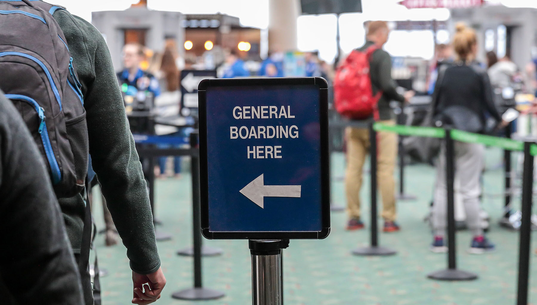 passengers lined up at airport security to the left of a sign showing them what to do.