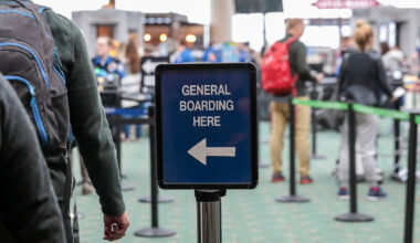 passengers lined up at airport security to the left of a sign showing them what to do.