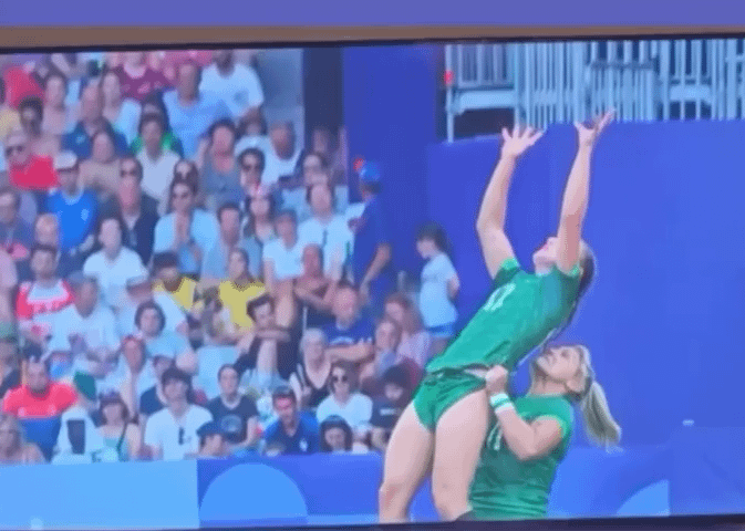 Woman on the Ireland Rugby team picking up one of her teammates to catch the ball