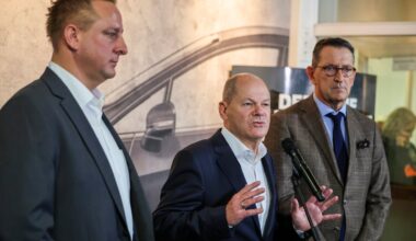 Bundeskanzler Olaf Scholz (SPD) steht zwischen dem Betriebsratschef von Ford Deutschland, Benjamin Gruschka (links), und dem Geschäftsführer der Ford Werke, Marcus Wassenberg (rechts).